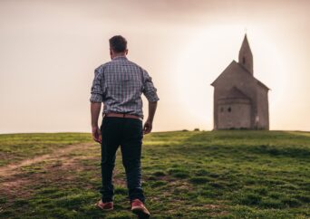 Man walks in field with chapel in the background.
