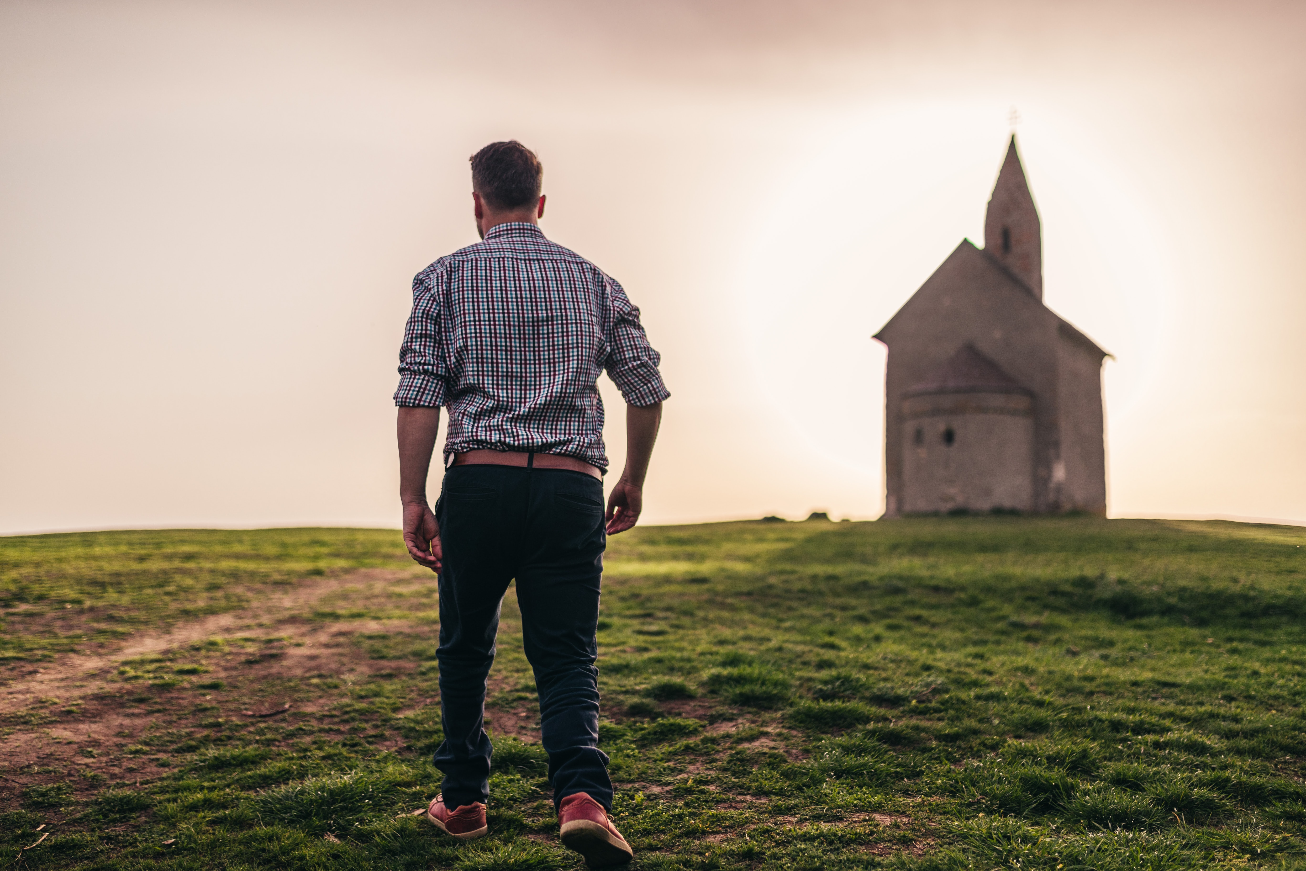 Man walks in field with chapel in the background.